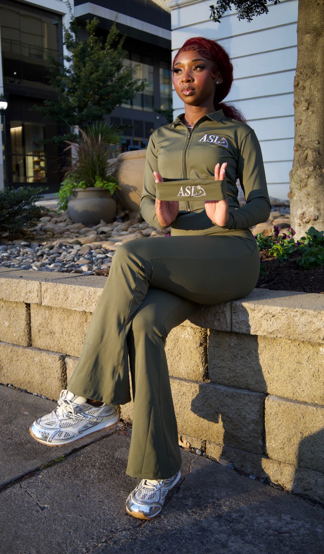Seated model wearing the ASL olive zip-up and flared pants